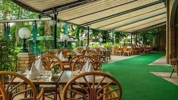 An outdoor dining area with tables and chairs, a green carpet, and a covered roof.