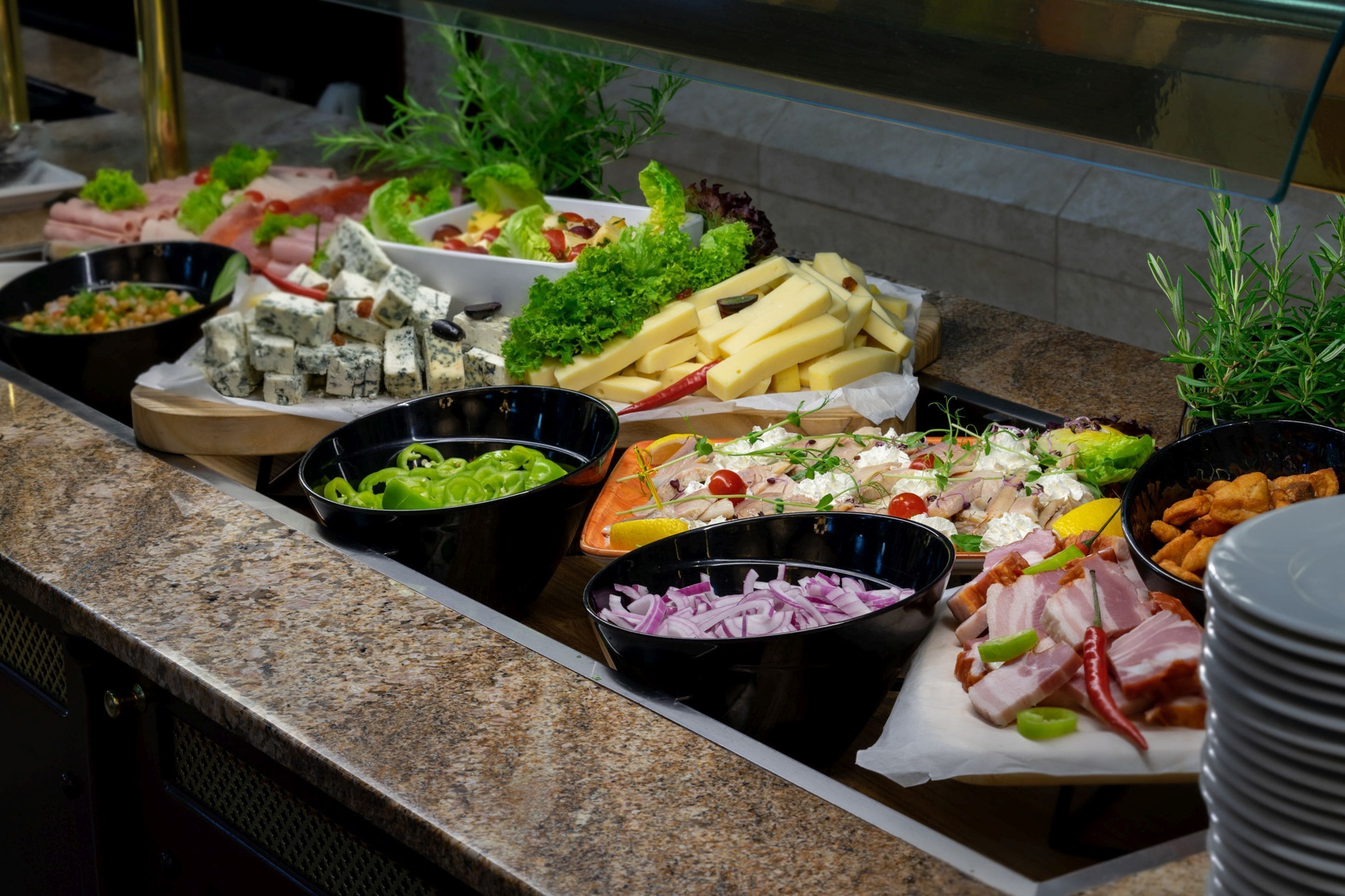 A buffet with various food items including cheese, meats, vegetables, and salads.