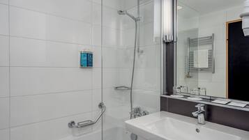 Un baño moderno con ducha envuelta en vidrio, un lavamanos blanco y un espejo grande.