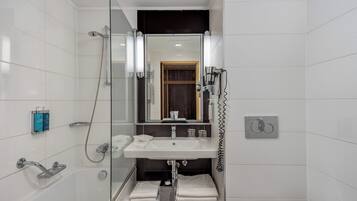 Un baño moderno con ducha envuelta en vidrio, un lavamanos blanco con espejo arriba y un inodoro.