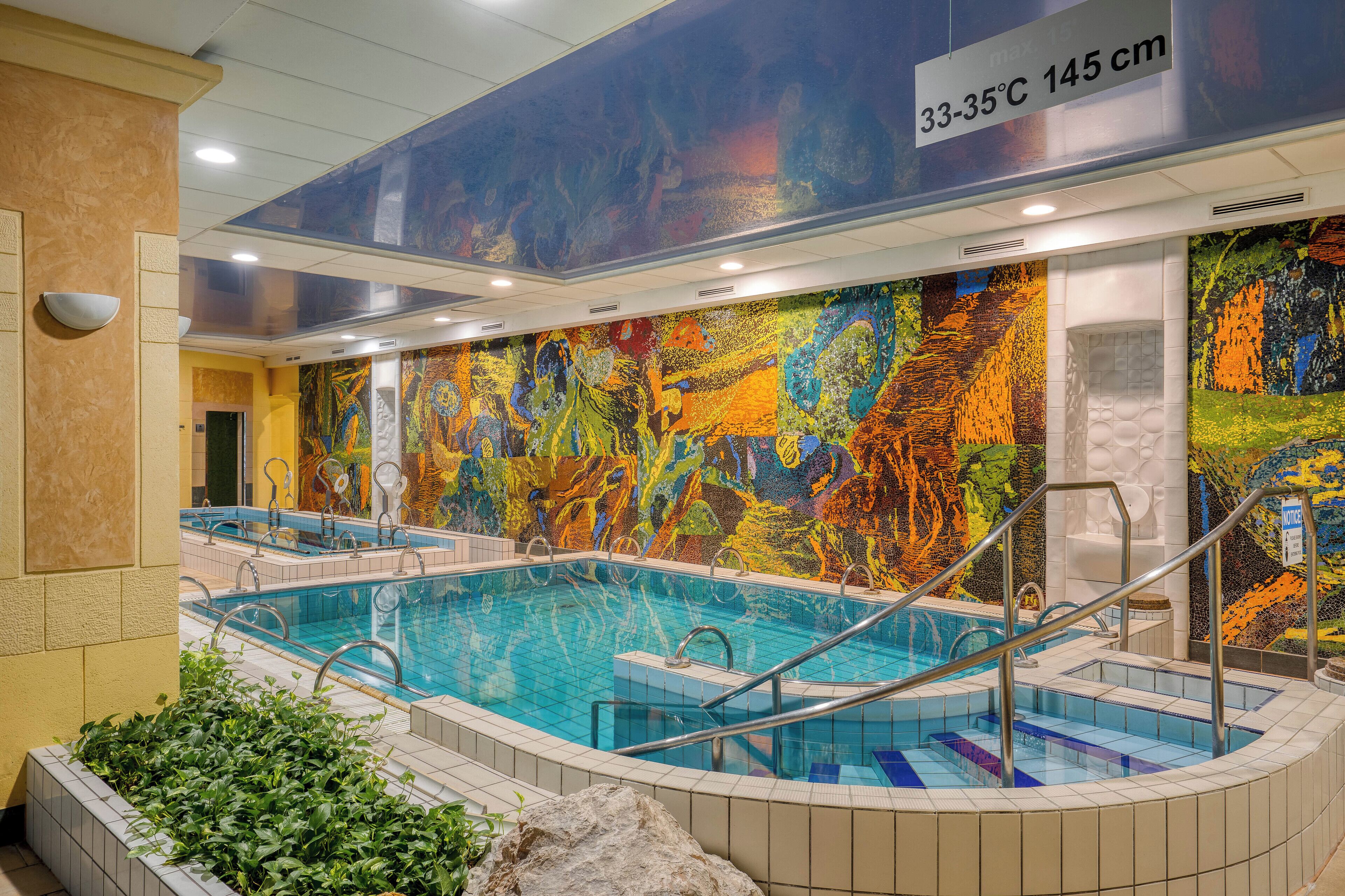 A swimming pool with a colorful mural, a temperature sign, and a spa area.