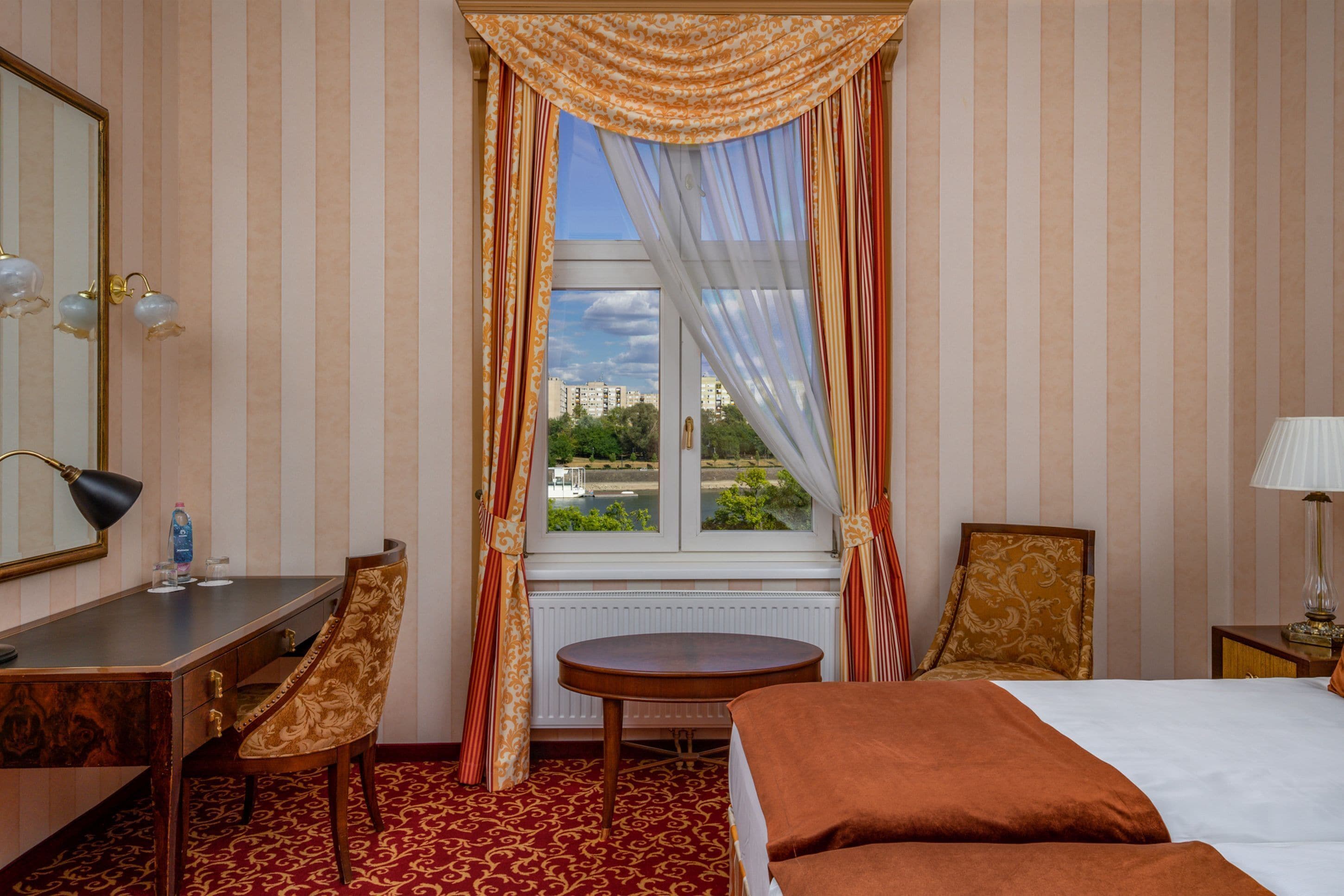 A hotel room with a bed, a desk, a chair, a round table, and a window with curtains.