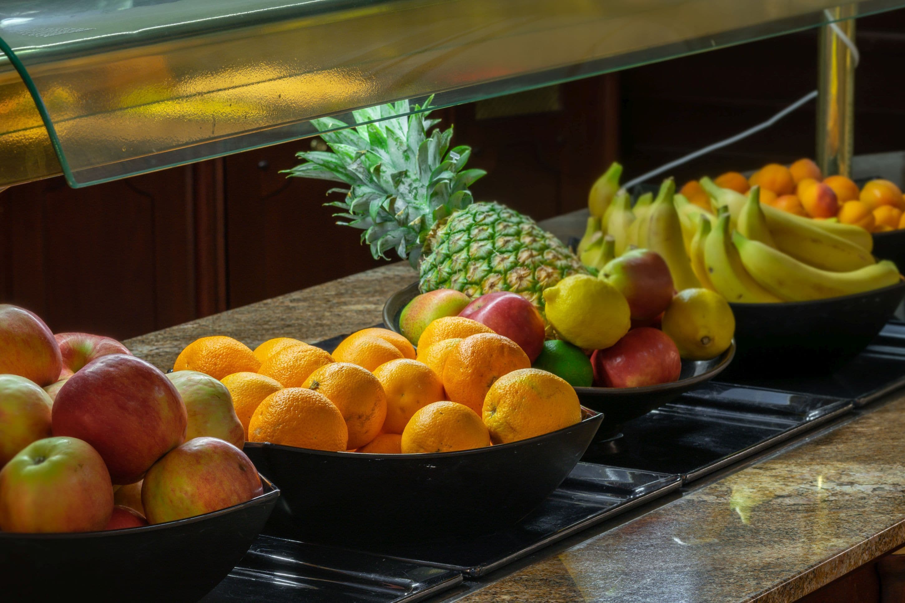 A buffet with various fruits including apples, oranges, bananas, and a pineapple.