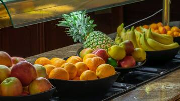 A buffet with various fruits including apples, oranges, bananas, and a pineapple.