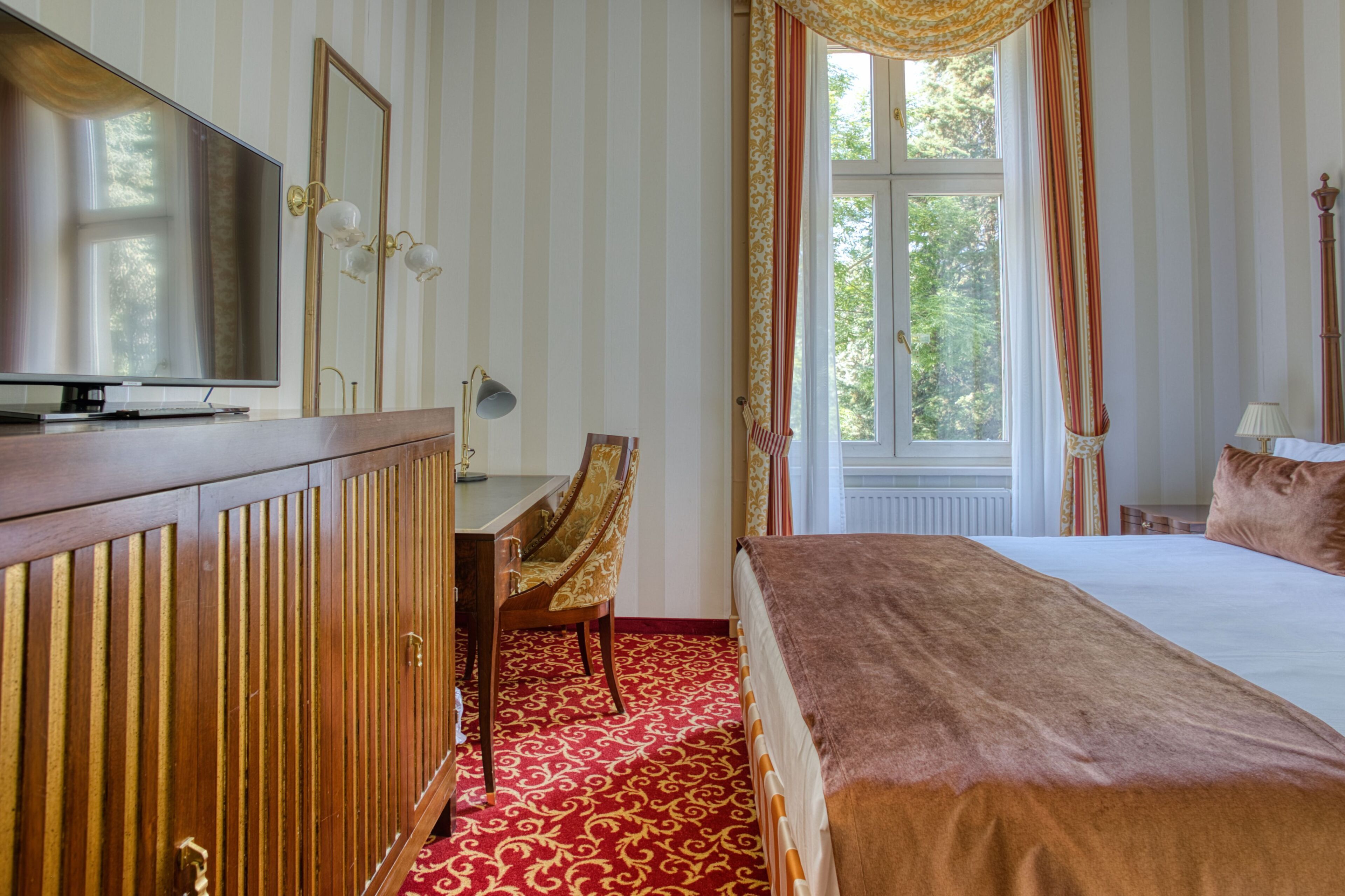 A hotel room with a bed, a desk, a television, a mirror, and a window with curtains.
