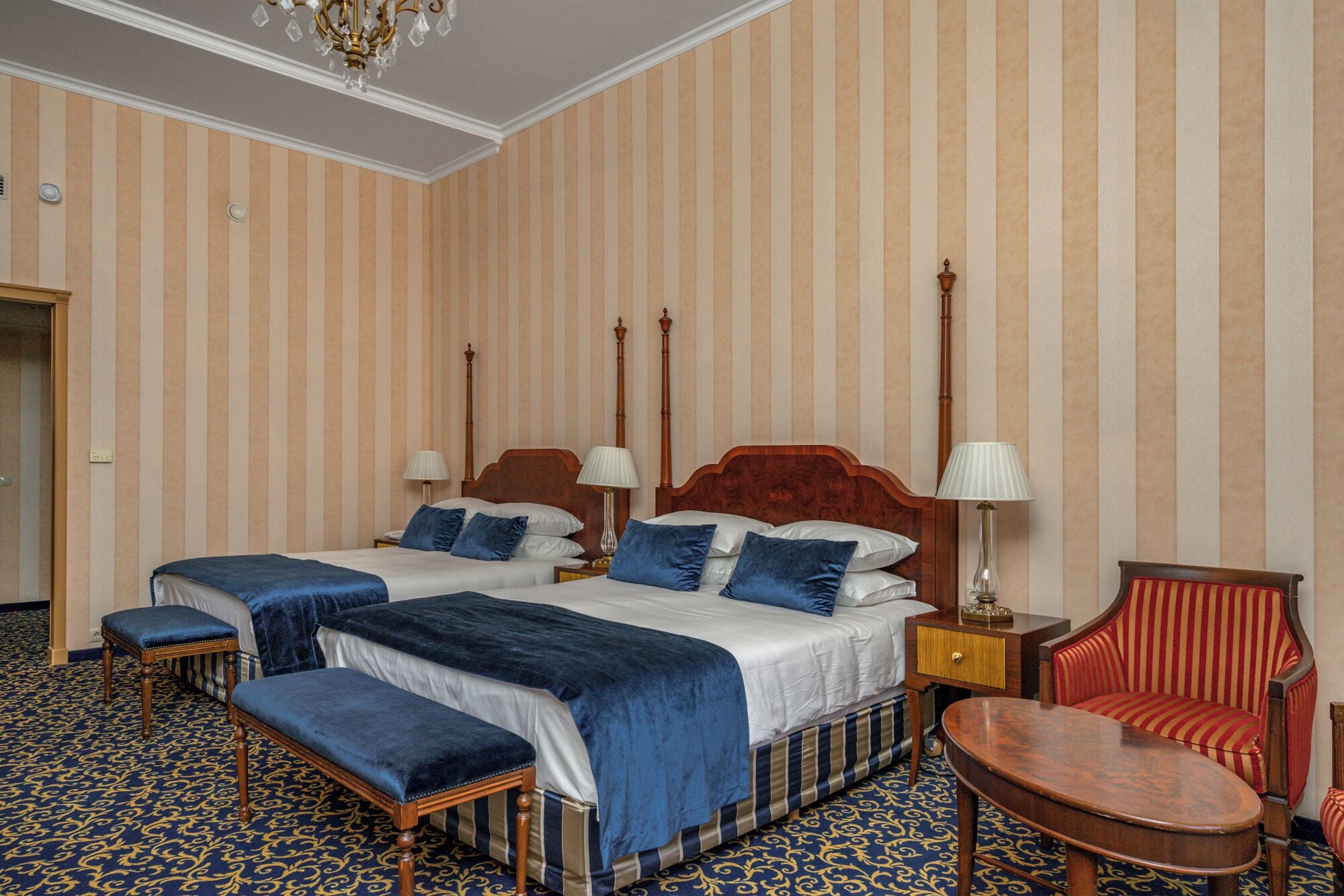 Quarto de hotel com duas camas, uma cadeira, uma mesa e um candelabro.
