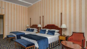 Quarto de hotel com duas camas, uma cadeira, uma mesa e um candelabro.