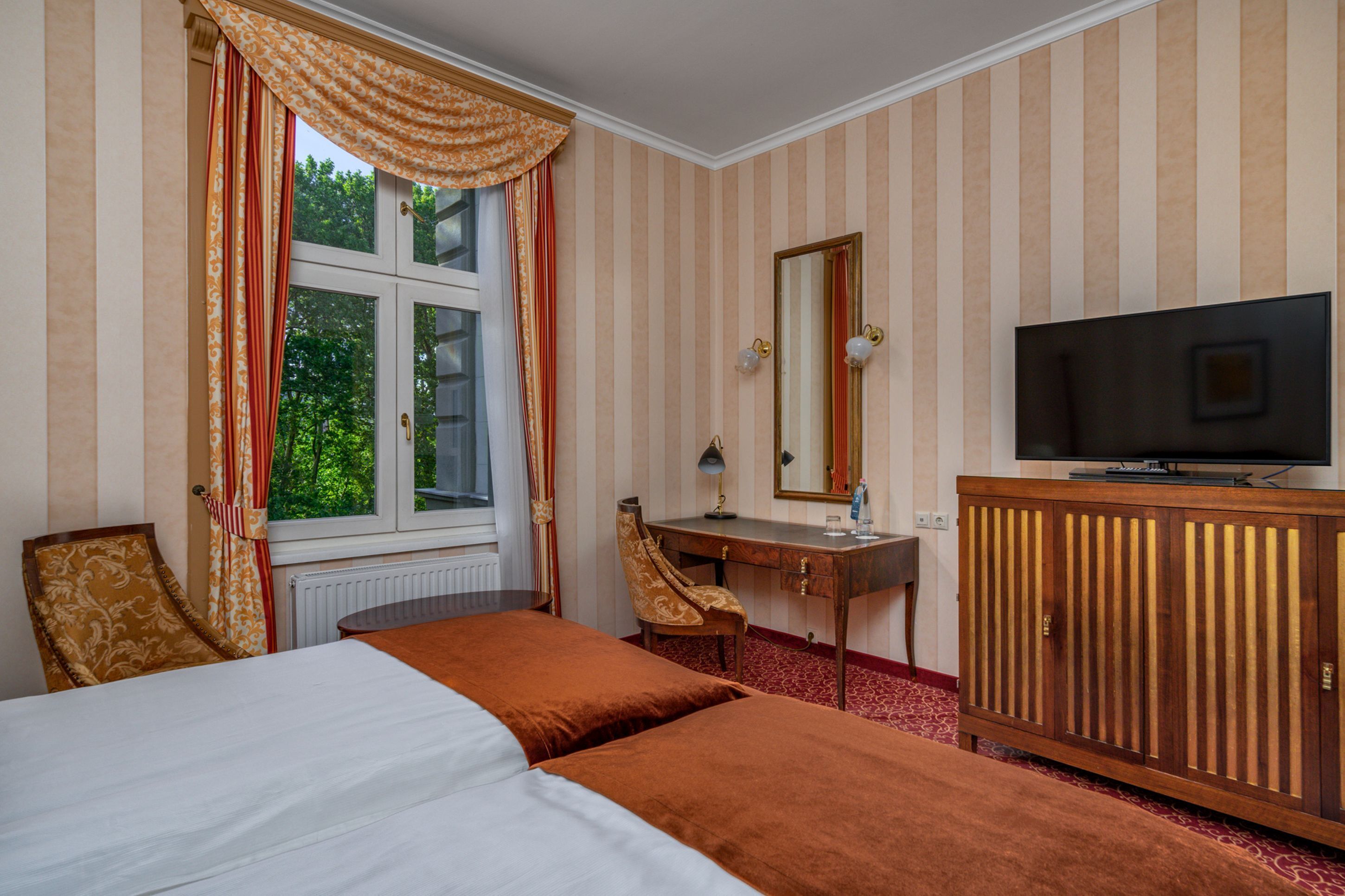 Una habitación de hotel con cama, escritorio, silla, televisor y ventana con cortinas.