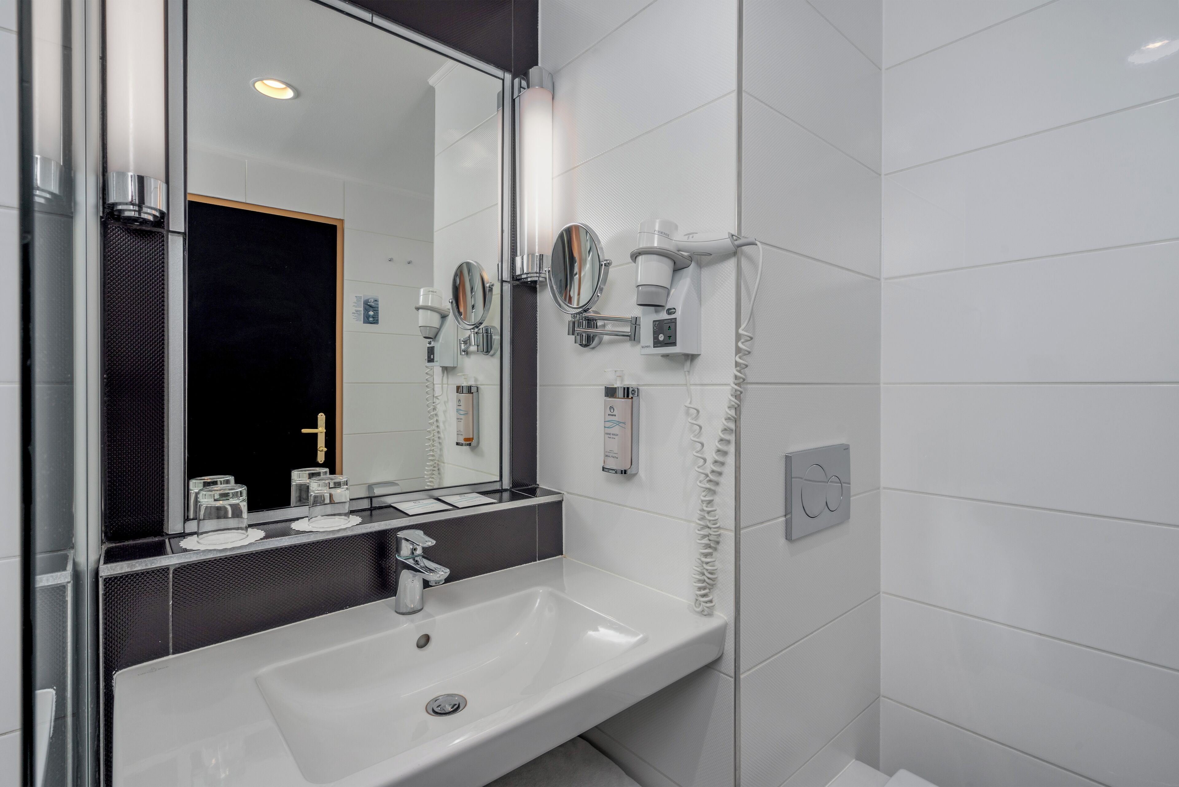 A modern bathroom with a white sink, a large mirror, and a hairdryer mounted on the wall.