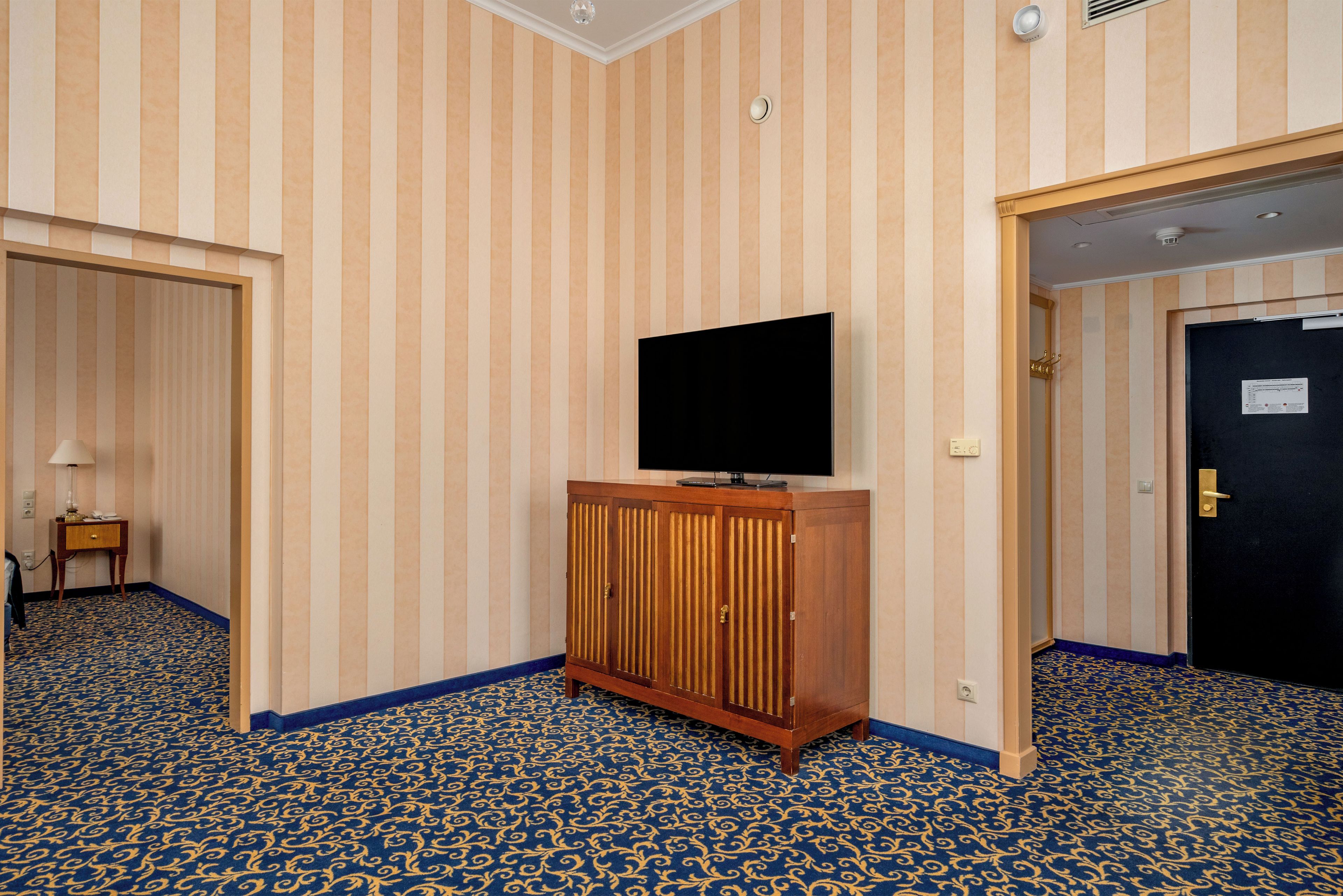 Una habitación de hotel con papel tapiz a rayas, un mueble de madera con un televisor de pantalla plana y una alfombra estampada.