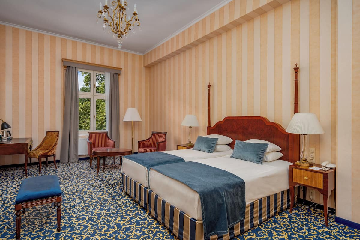Ein Hotelzimmer mit gestreifter Tapete, einem großen Bett mit zwei Kissen, einem Nachttisch, einem Sessel und einem Schreibtisch.