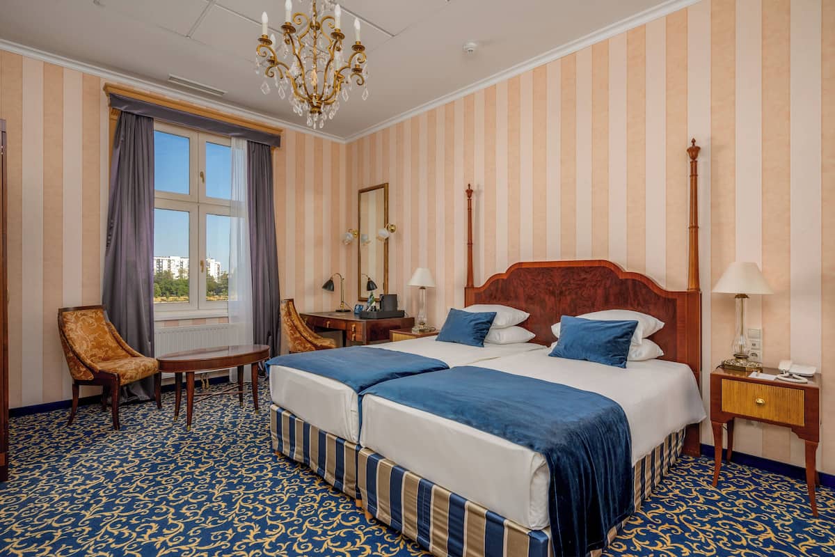 Ein Hotelzimmer mit zwei Betten, einem Sessel, einem Schreibtisch, einem Spiegel und einer Deckenleuchte.