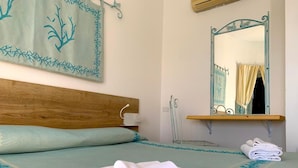 Una cama bien hecha con cabecera de madera, una mesita de noche con lámpara, un espejo con marco decorativo y una toalla doblada sobre la cama.