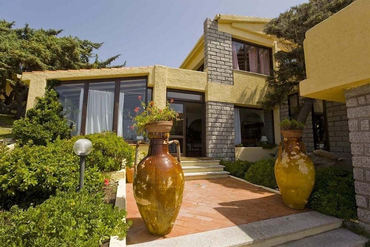 A modern two-story house with a brick facade, large windows, and a well-maintained garden with potted plants and a lamp post.