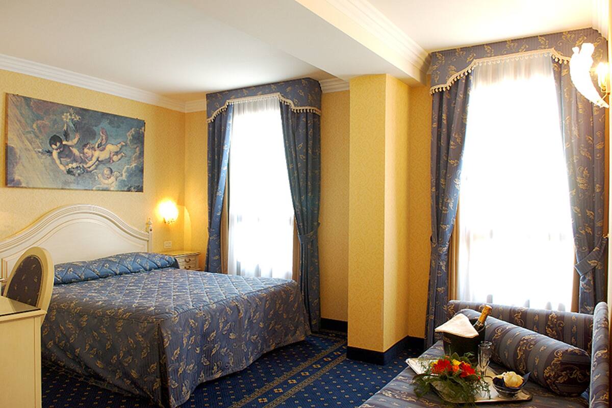 A hotel room with a bed, a sofa, a nightstand, a lamp, and a painting on the wall.