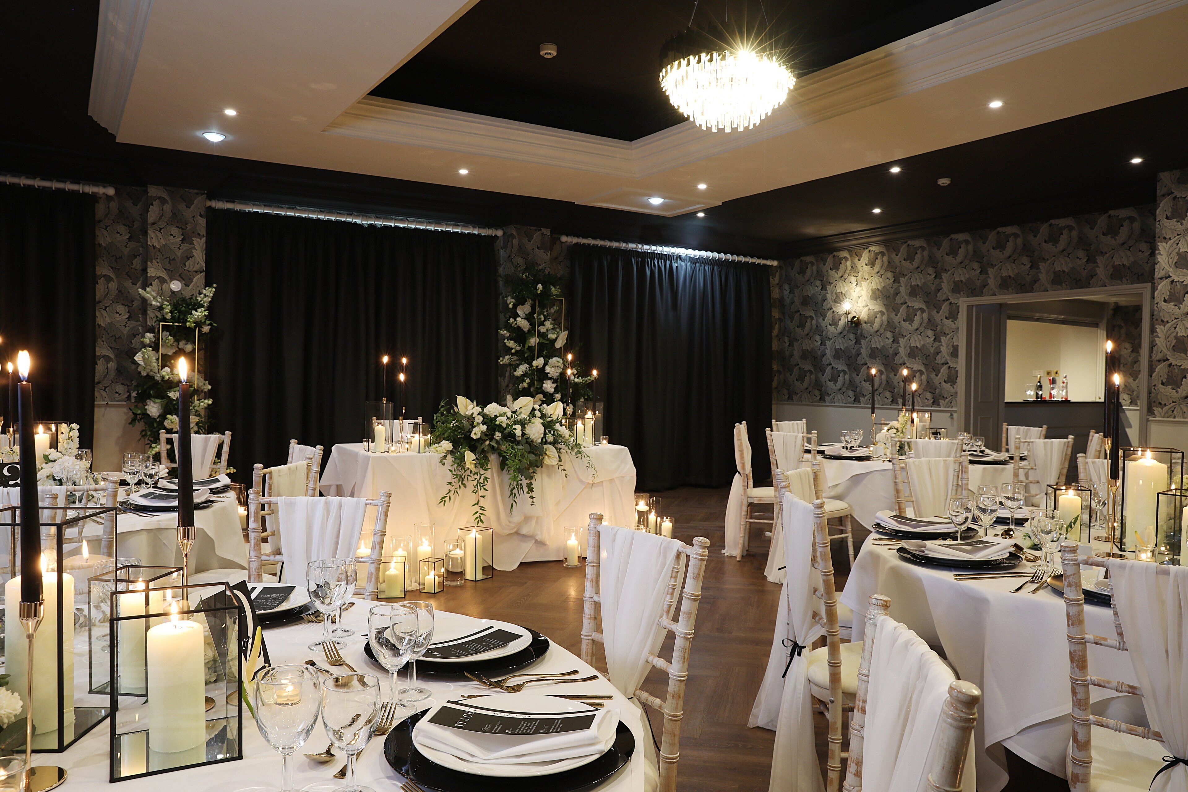 A banquet hall with round tables set for a formal event, featuring white tablecloths, candles, and floral centerpieces.