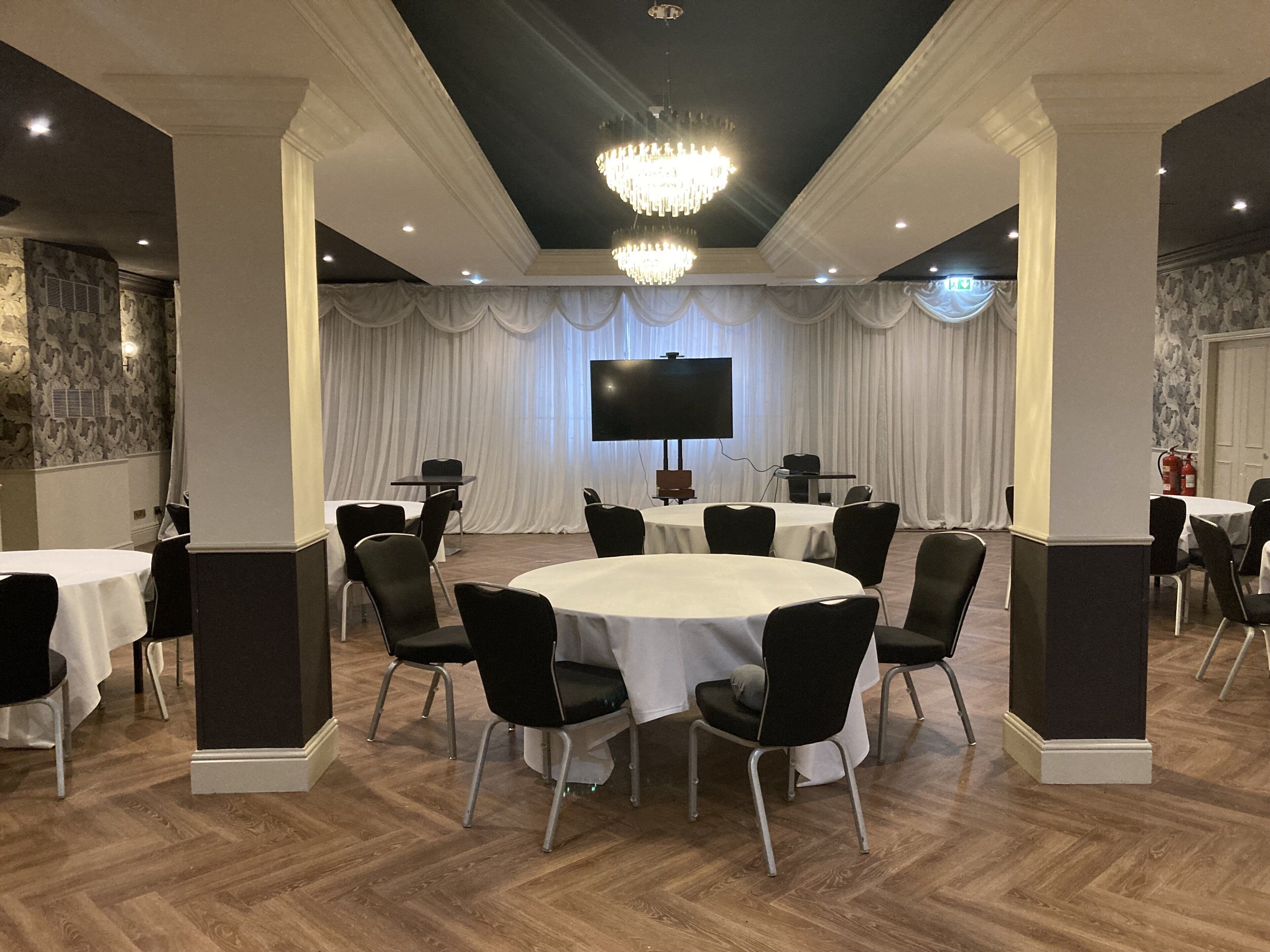 A conference room with round tables, black chairs, a large screen, and a chandelier.