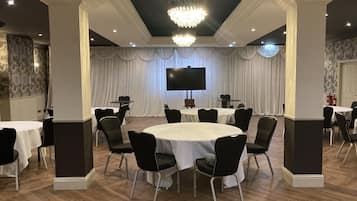 A conference room with round tables, black chairs, a large screen, and a chandelier.