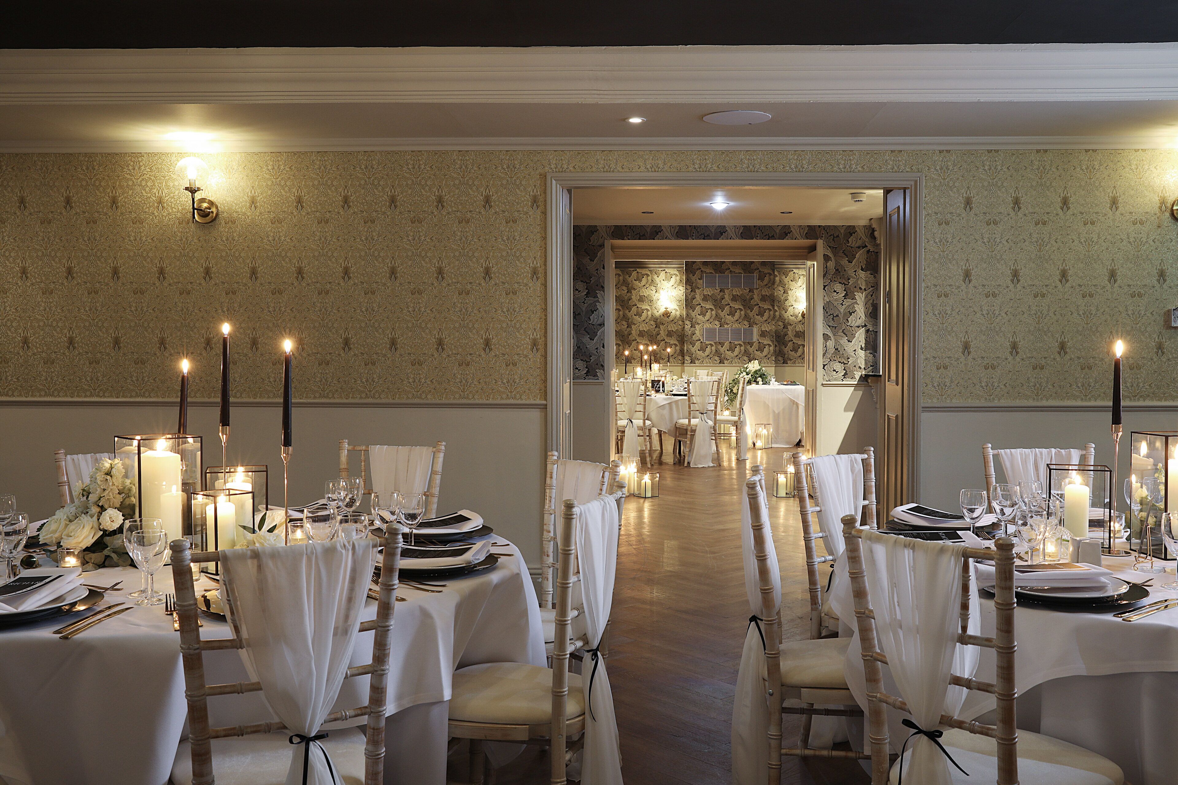 Une salle à manger élégante, avec des tables dressées pour le repas, agrémentée de centres de table illuminés par des bougies et de nappes blanches.