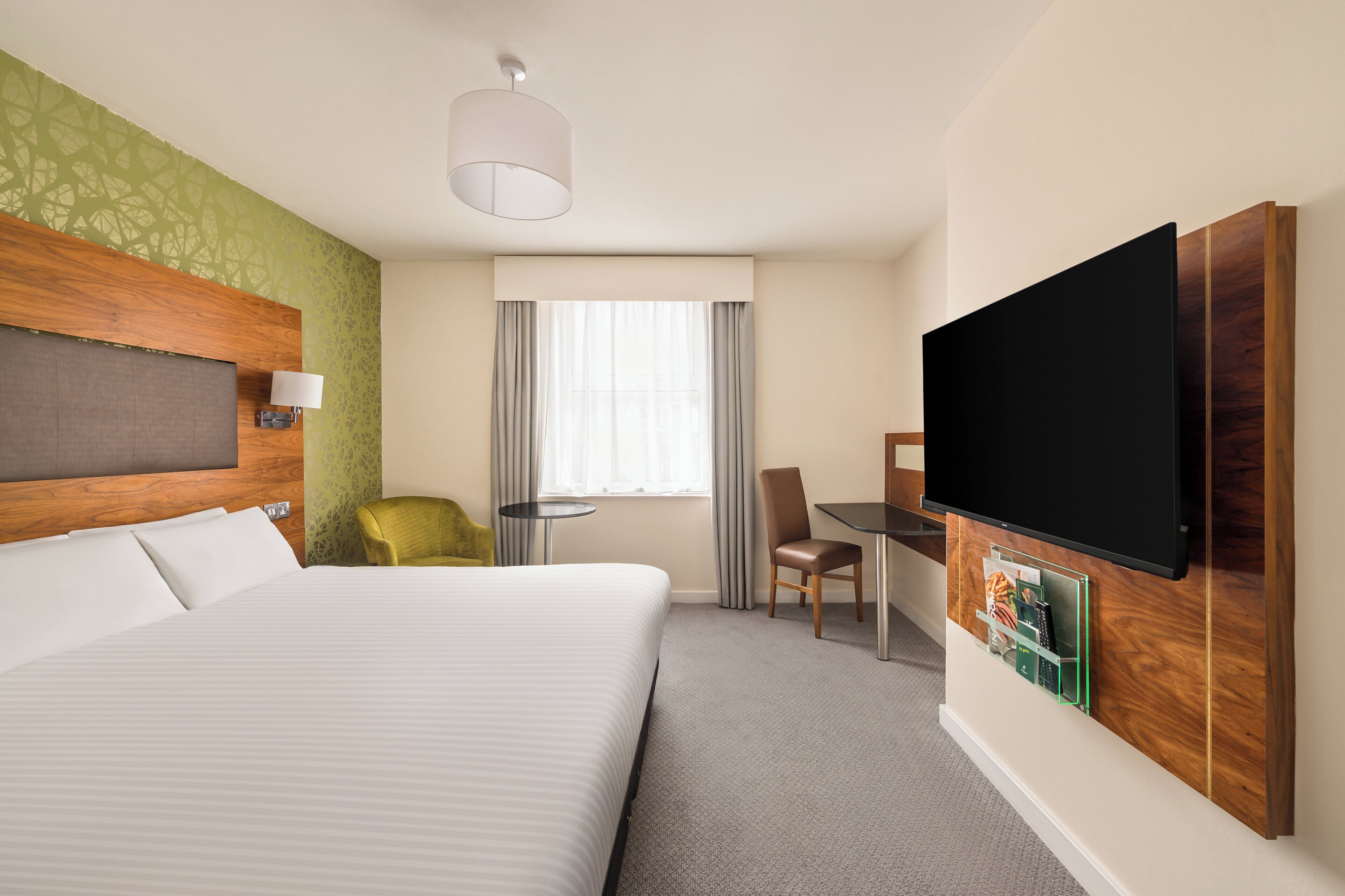 Habitación de hotel con una cama grande, un escritorio con silla, televisión y una ventana con cortinas.