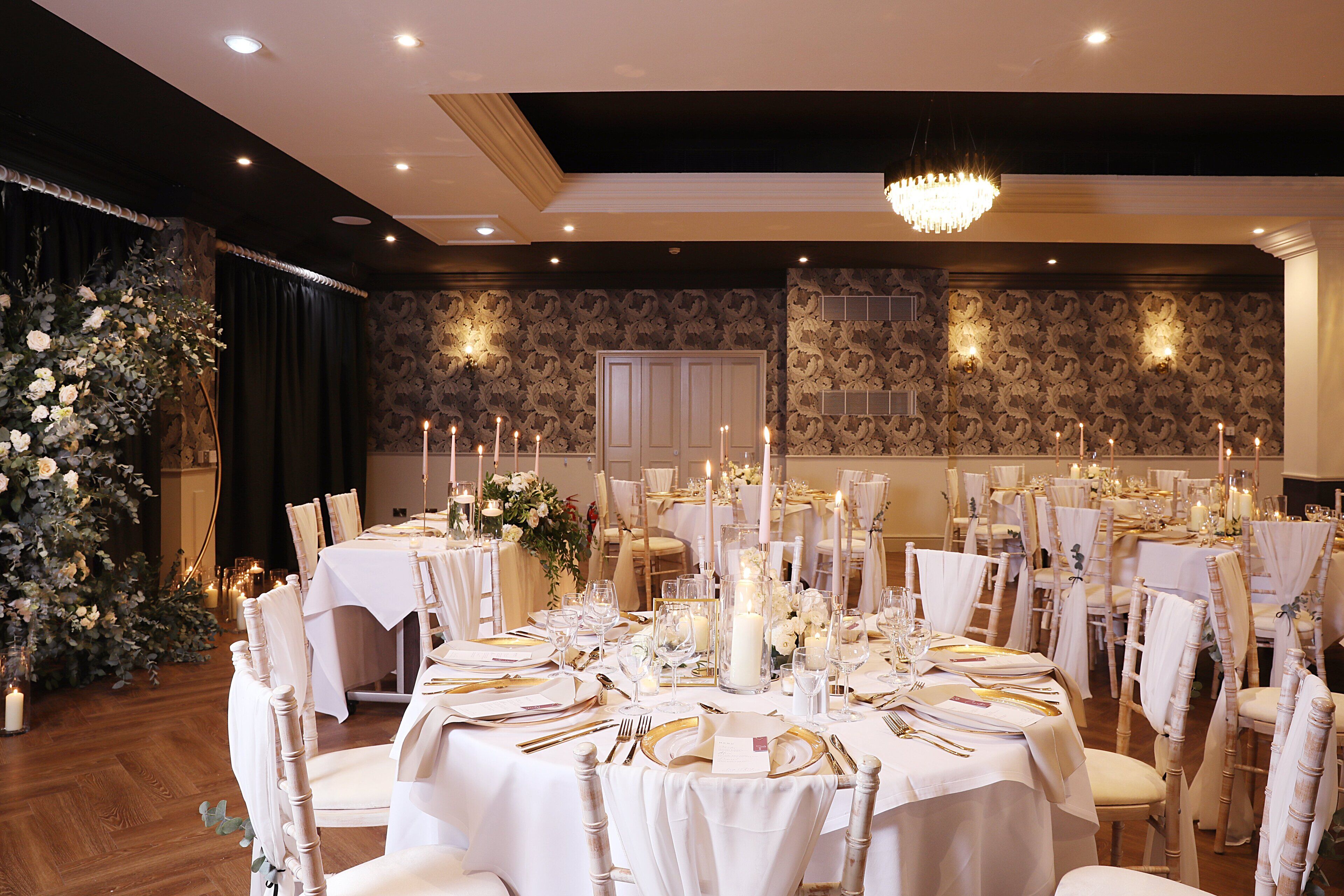 A banquet hall with round tables set for a formal event, featuring white tablecloths, candles, and floral centerpieces.