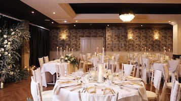 A banquet hall with round tables set for a formal event, featuring white tablecloths, candles, and floral centerpieces.