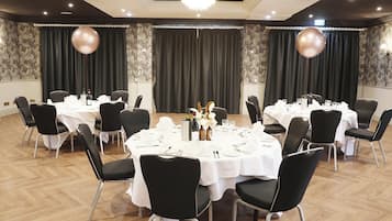 A conference room with multiple tables set for a meeting, each with chairs, white tablecloths, and centerpieces.