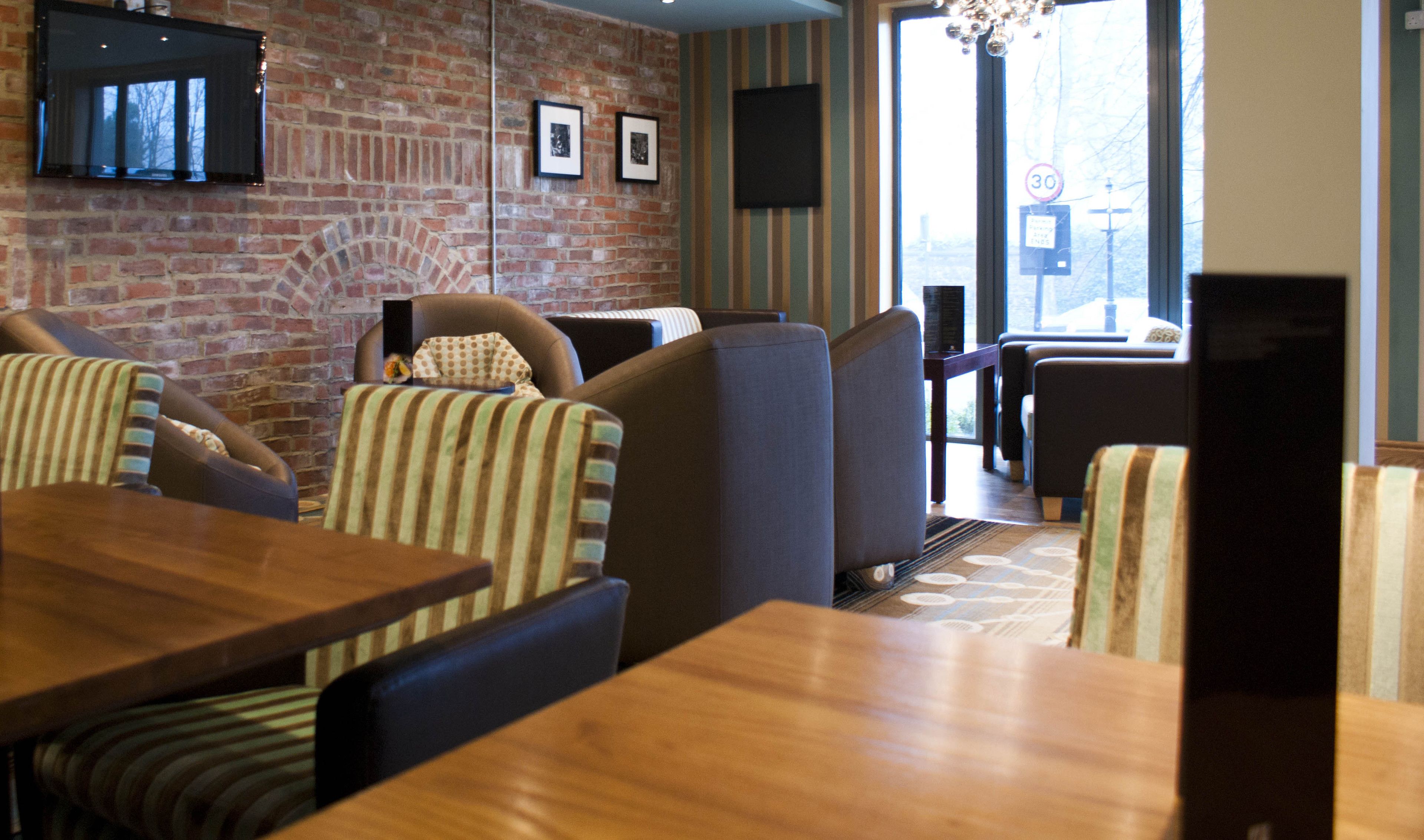 A restaurant with brick walls, striped upholstered chairs, and wooden tables.