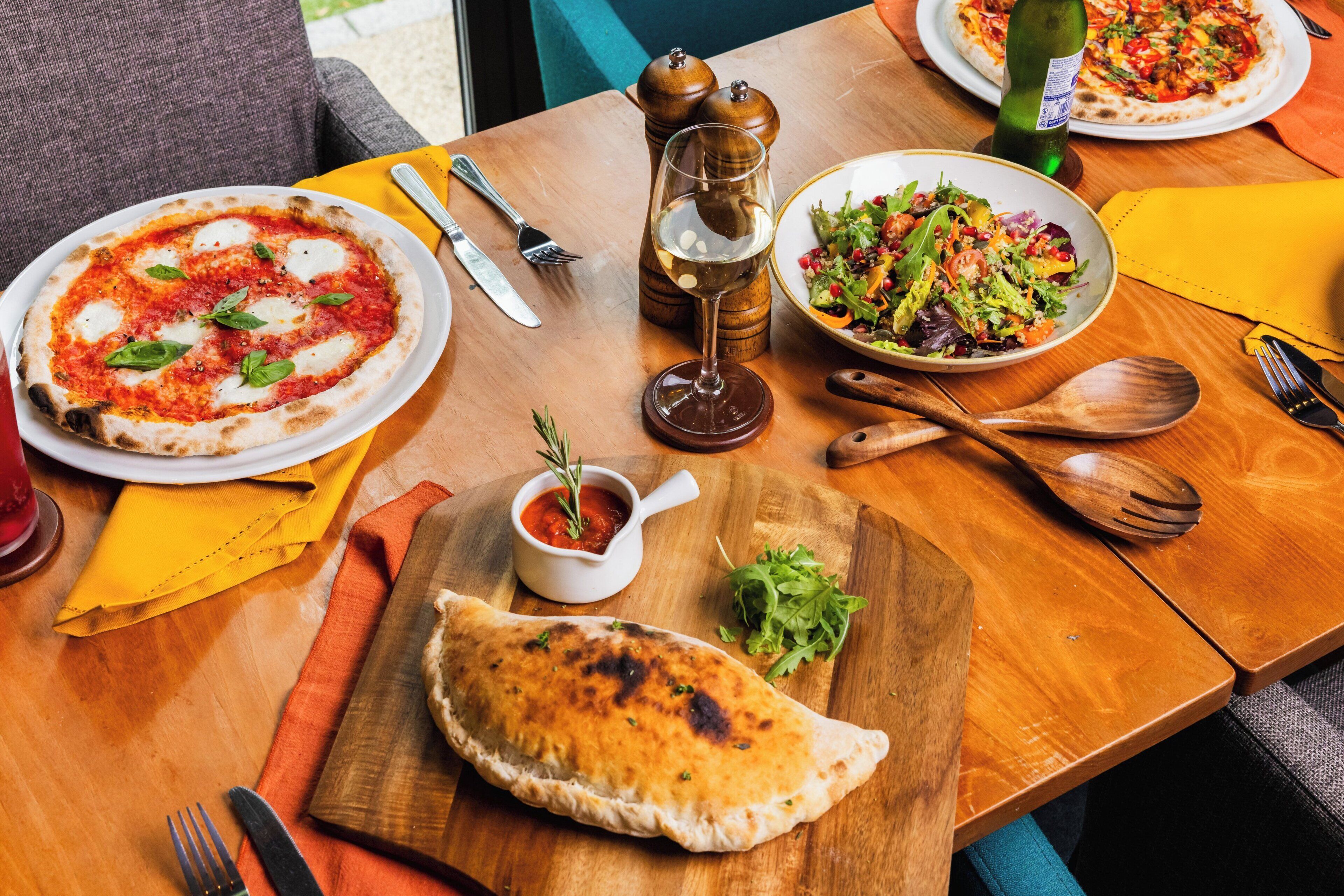 Une table en bois avec une pizza, une salade et un petit pain.