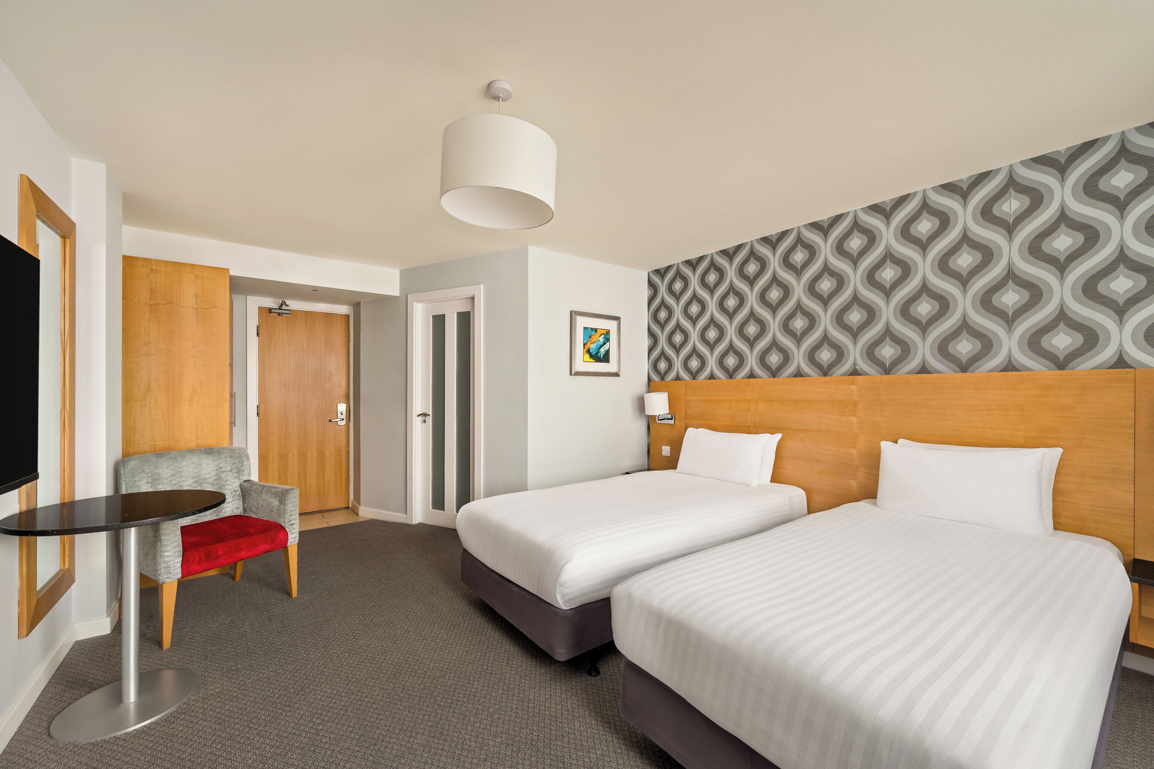 A hotel room with two beds, a small table, a chair, and a TV.