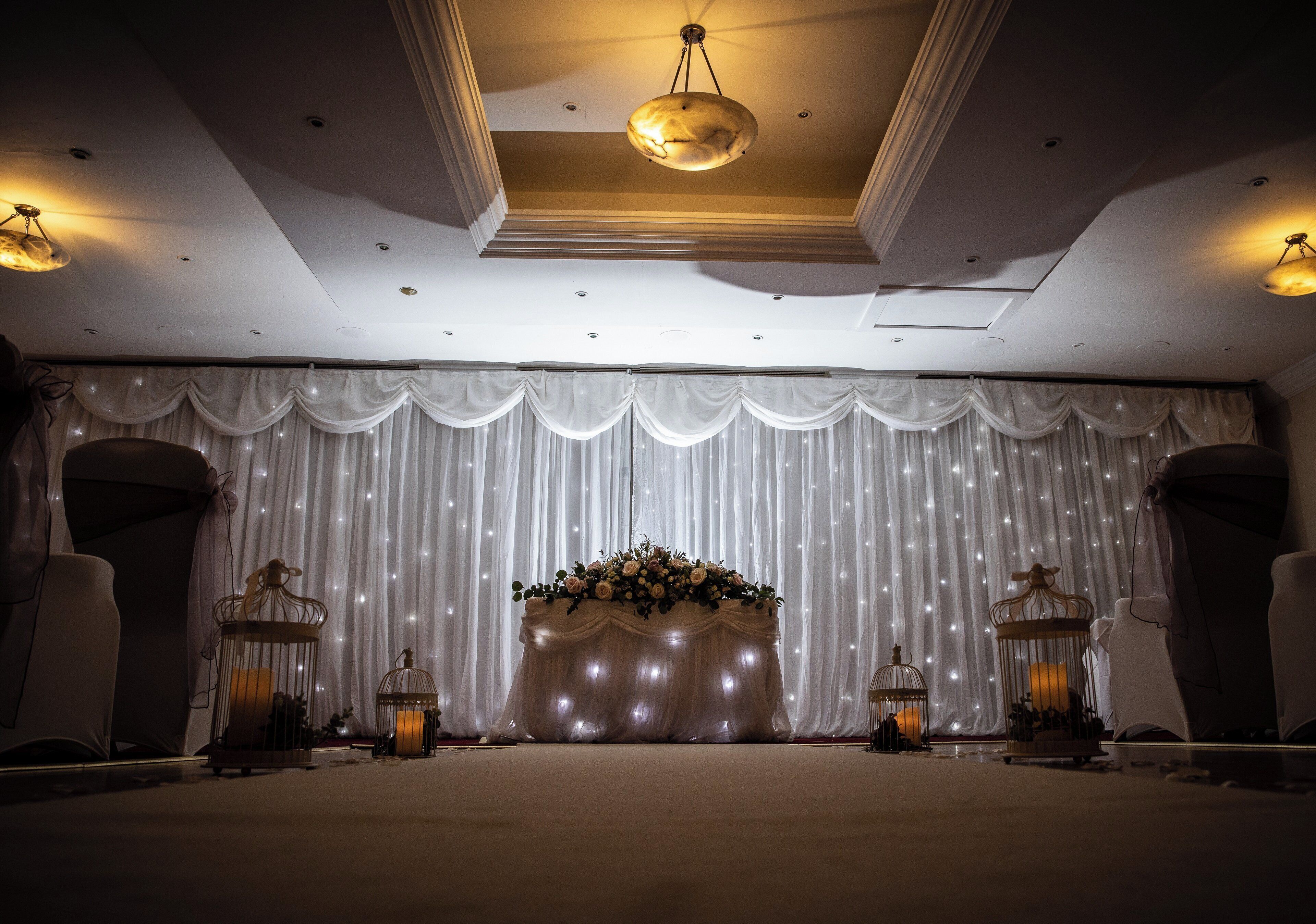 A stage with draped curtains and a floral arrangement, flanked by candle holders.