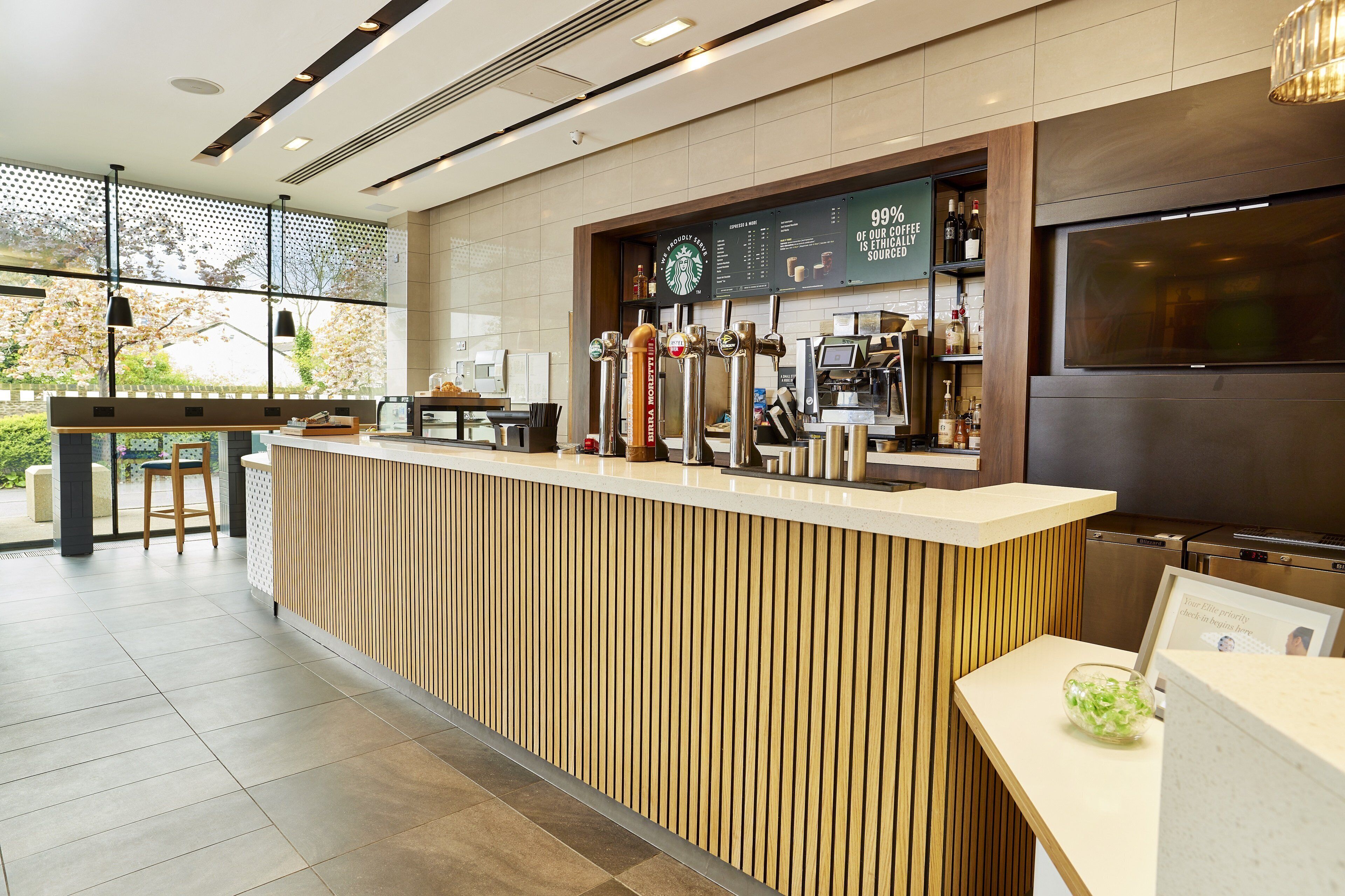 A modern coffee shop interior with a wooden counter, espresso machines, and a menu board.