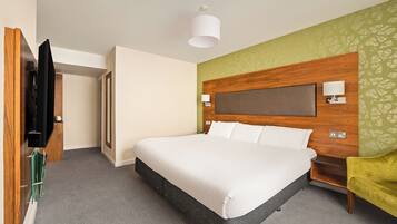Habitación de hotel con una cama grande, cabecera de madera, televisión y una pared verde decorativa.
