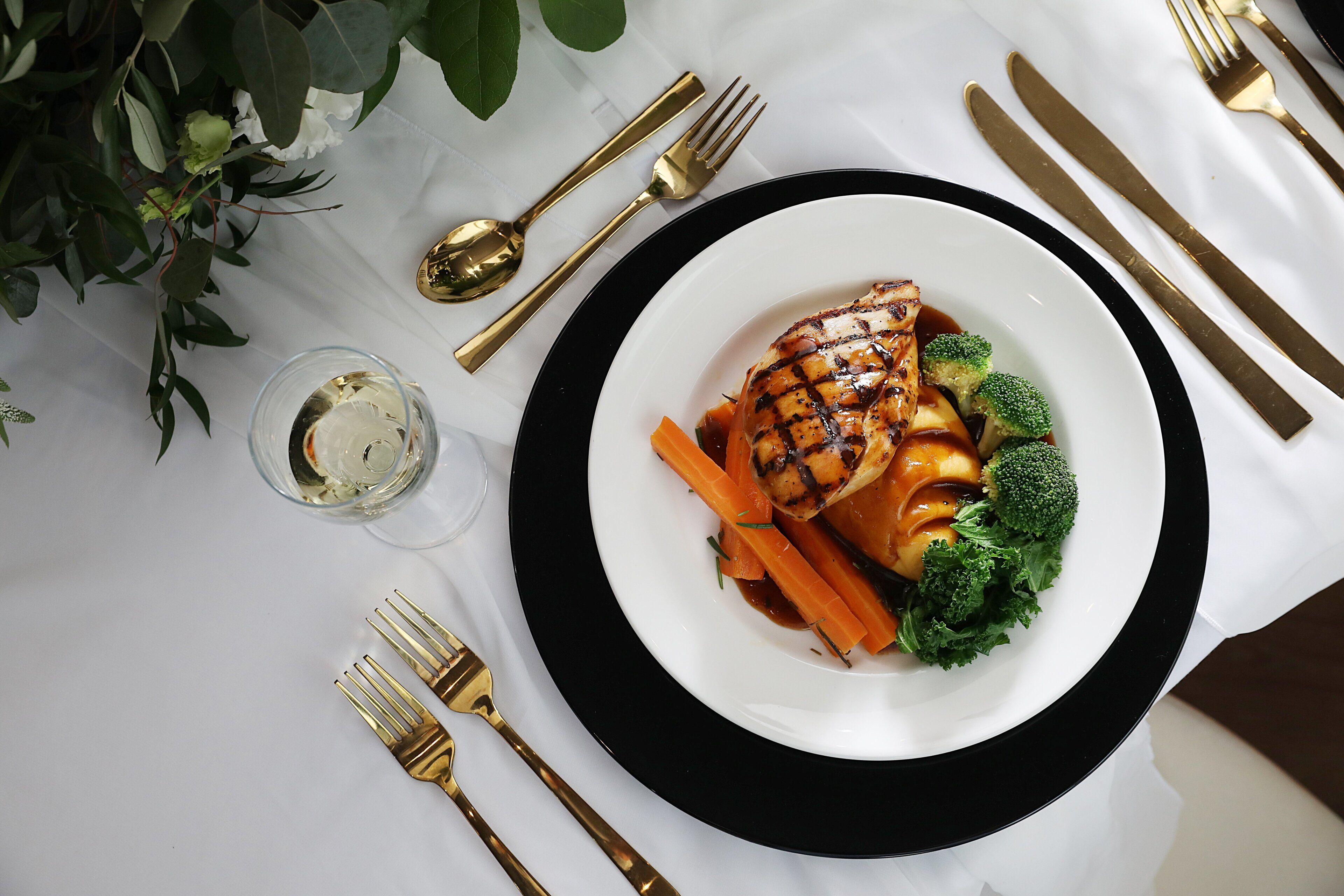 Une table blanche avec une assiette à bordure noire contenant du poulet grillé, des carottes et des brocolis.