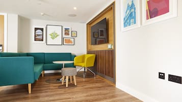 A modern living room with a teal sofa, a yellow chair, a round table, and framed artwork on the walls.