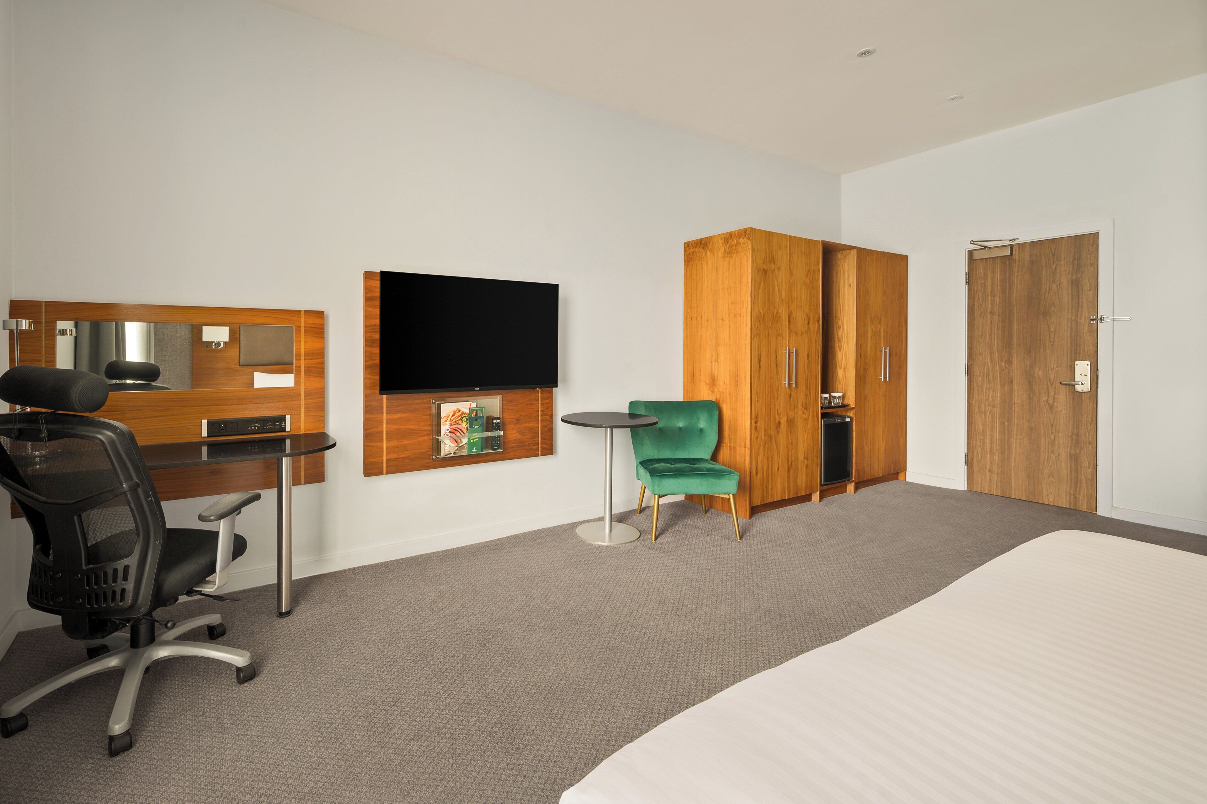 A hotel room with a bed, a desk with a chair, a television, a wardrobe, and a small table with a chair.