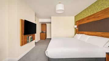 A hotel room with a large bed, a flat-screen TV mounted on the wall, a wooden headboard, and a small bedside table.