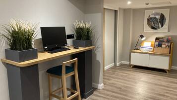 A modern home office with a wooden desk, two potted plants, a computer, and a printer.