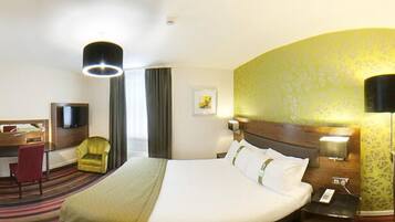 A hotel room with a large bed, a desk with a chair, a television, and a lamp.