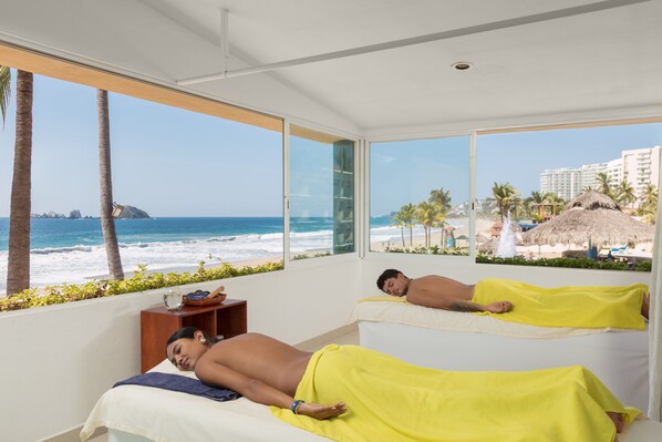 A room with two beds, large windows with a beach view, and a small wooden side table. - Posada Real Ixtapa (Ixtapa)