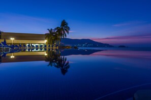 A poolside area with lounge chairs and a palm tree, reflecting the surrounding lights and sky.