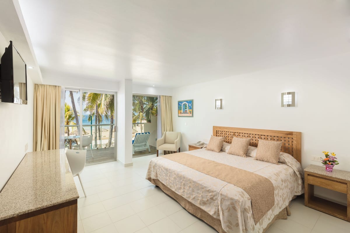 A hotel room with a bed, a desk, a chair, and a view of the beach.