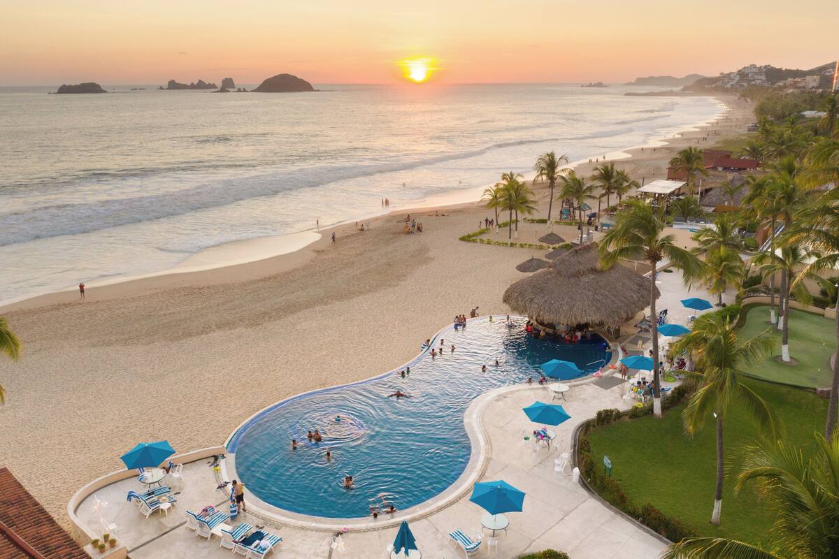 A resort with a swimming pool, beach, and sunset view.