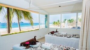 Una habitación con dos camas, amplias ventanas y vista a la playa, decorada con motivos tropicales.