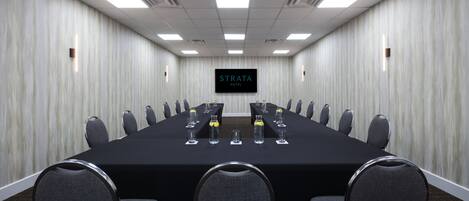 Un salón de conferencias con una larga mesa, varias sillas y una pantalla de televisión que muestra