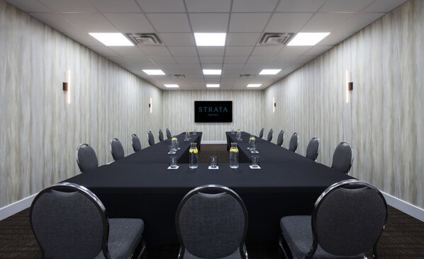 Un salón de conferencias con una larga mesa, varias sillas y una pantalla de televisión que muestra