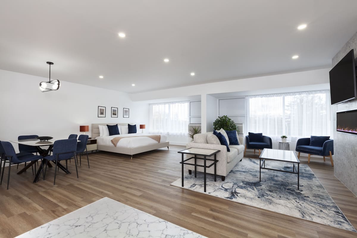 A modern living room with a sofa, coffee table, and chairs, a dining area with a table and chairs, and a large TV mounted on the wall.