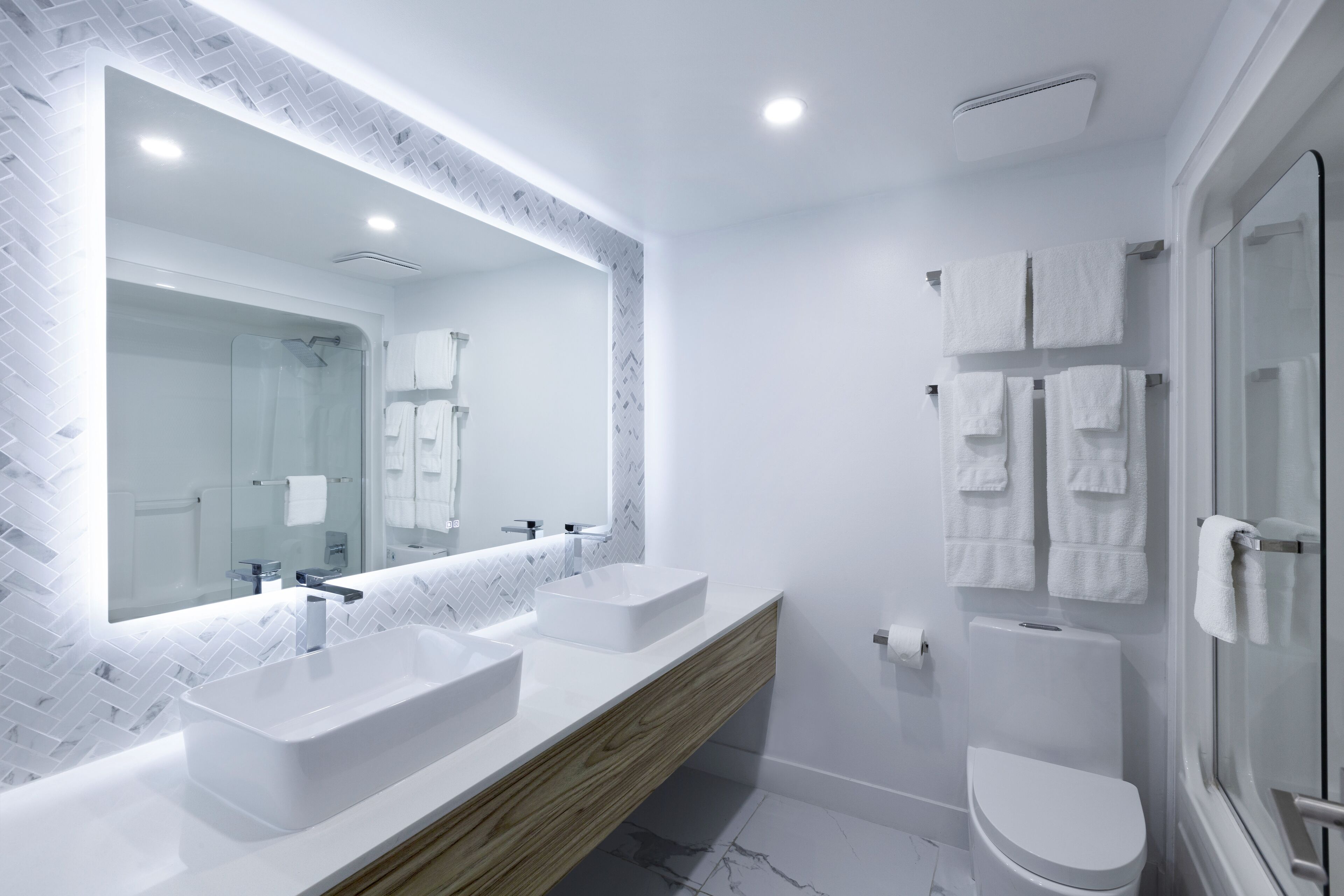 Un baño moderno con dos lavamanos, un espejo grande y una cabina de ducha de vidrio.