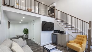 Un salon moderne avec un canapé, un fauteuil jaune, une table basse en marbre et un escalier menant à un niveau supérieur.