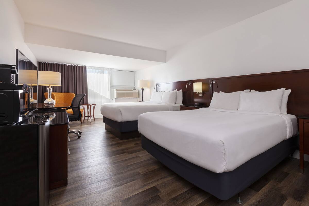 A hotel room with two beds, a desk with a computer, a chair, and a small table.